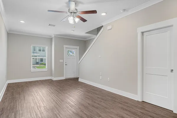 an empty room with wooden floor chandelier fan and windows