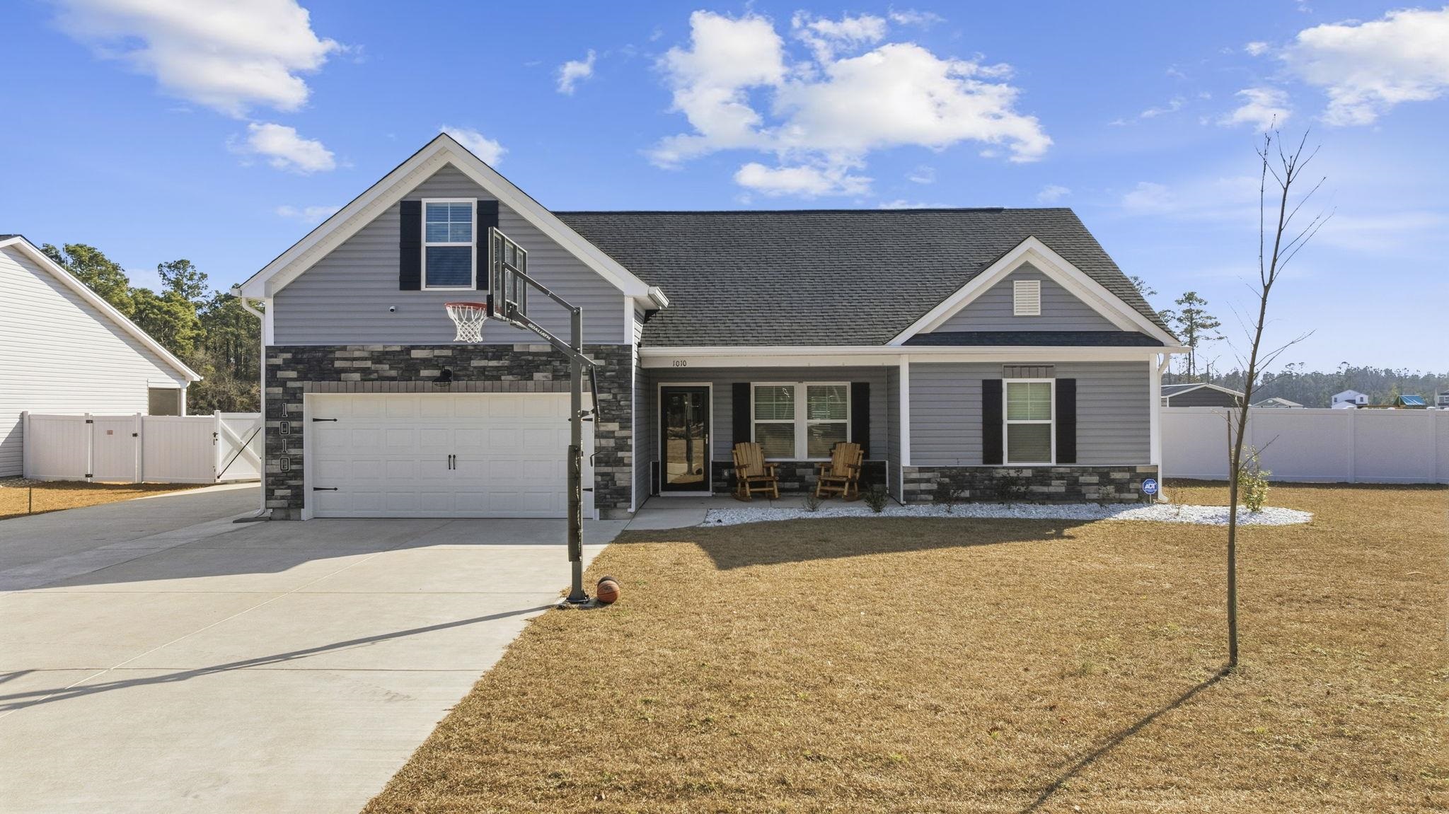 Traditional-style home featuring stone siding, a gate, driveway, an attached garage, and a shingled roof