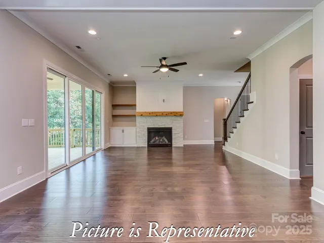 a view of an empty room with wooden floor a ceiling fan and a fireplace