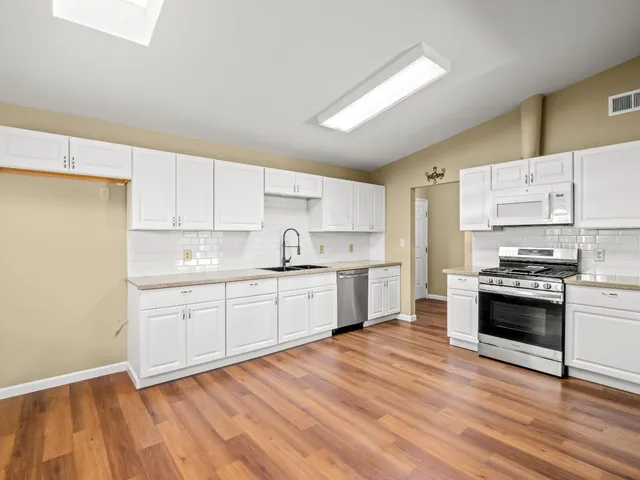 a kitchen with stainless steel appliances granite countertop a stove top oven a sink dishwasher and a refrigerator with wooden floor