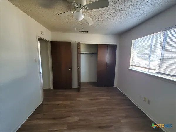 an empty room with wooden floor chandelier fan and windows