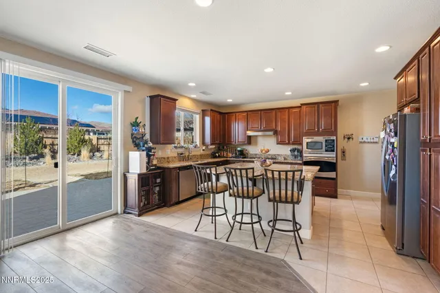 a kitchen with stainless steel appliances kitchen island granite countertop a refrigerator a stove a sink a dining table and chairs with wooden floor