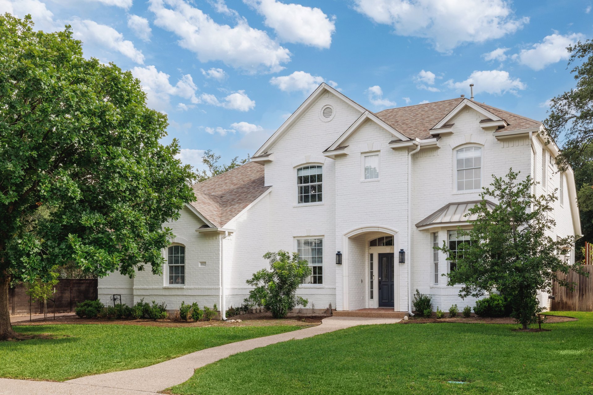 White brick home with a charming front porch welcomes visitors up a graceful winding pathway.