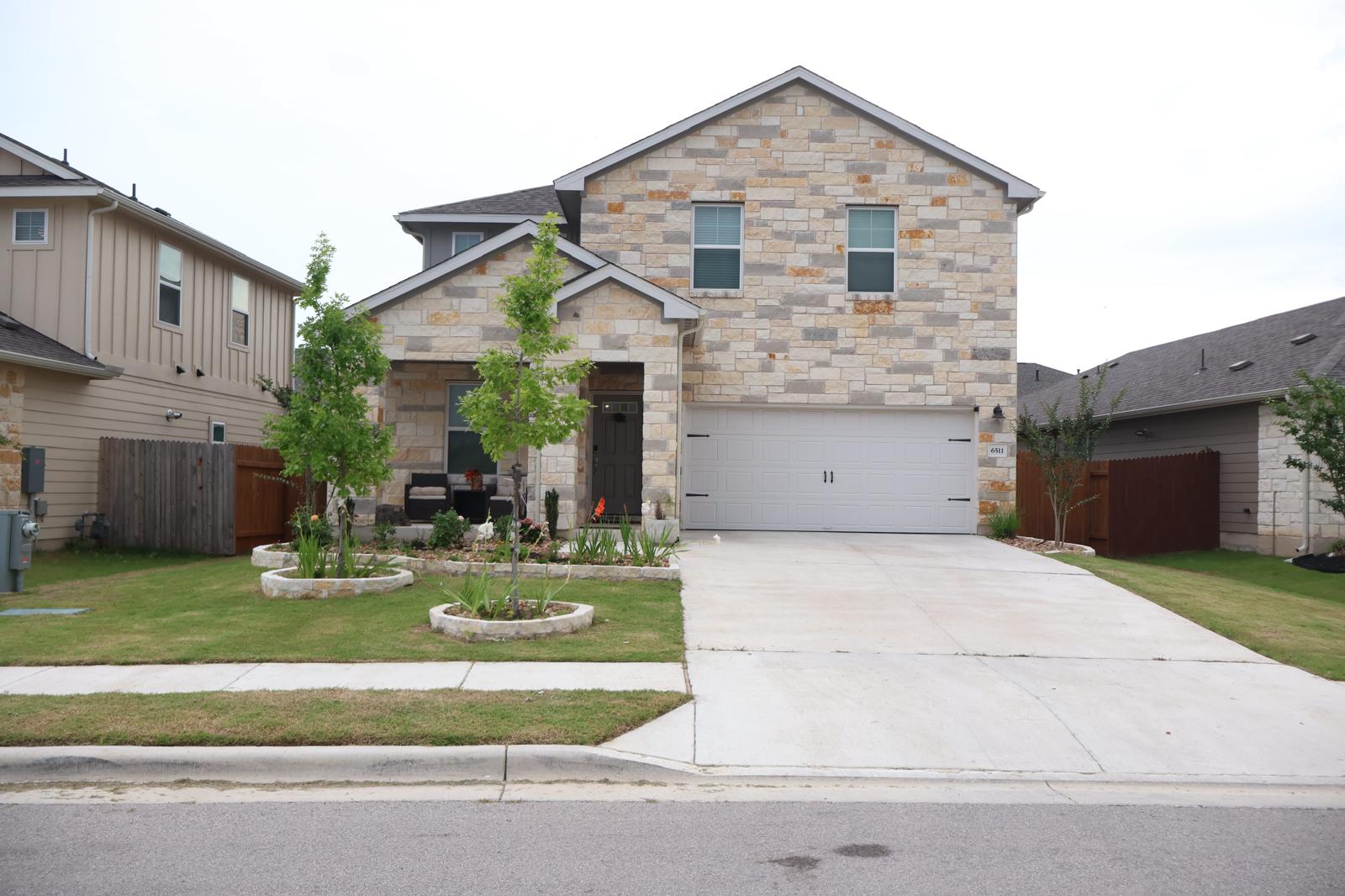 6511 Dragride Road Buda, TX 78610 - Photo 2 of 36 A welcoming stone facade home with well-maintained landscaping and a spacious driveway.