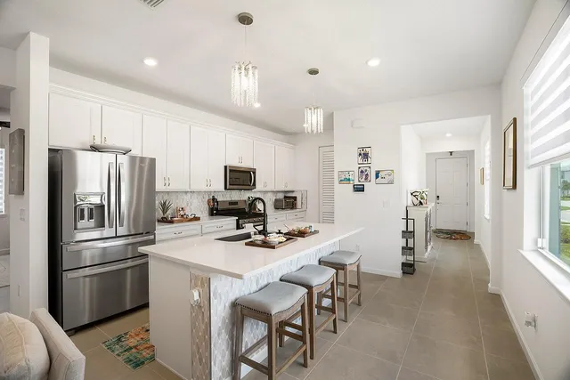 a kitchen with stainless steel appliances kitchen island granite countertop a stove a sink a refrigerator and white cabinets with wooden floor