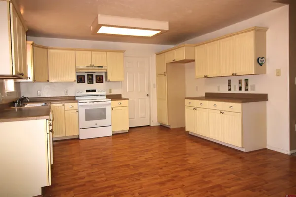 a kitchen with a stove a sink white cabinetry and wooden floor