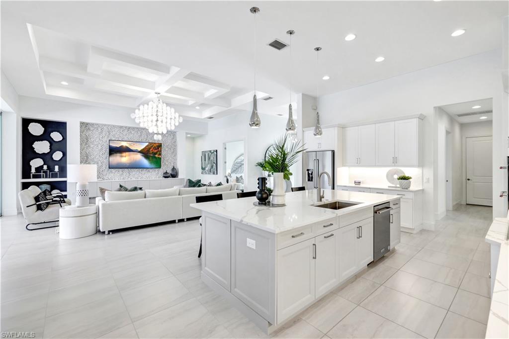 8912 Nevis Way Naples, FL 34112 - Photo 10 of 45 Kitchen featuring white cabinetry, coffered ceiling, decorative light fixtures, a kitchen island with sink, and light stone countertops