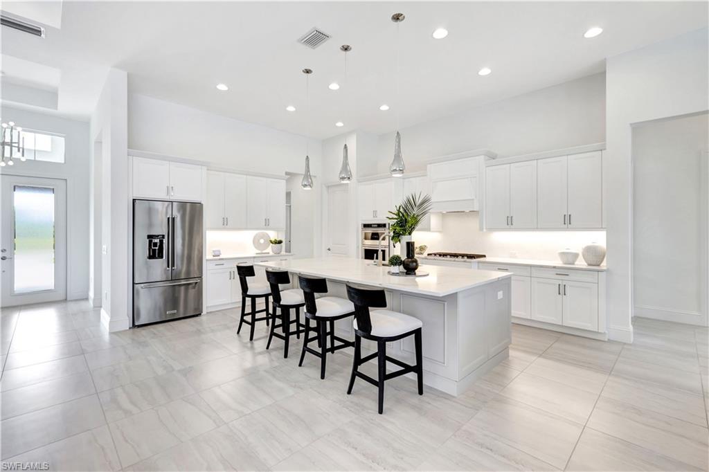 8912 Nevis Way Naples, FL 34112 - Photo 9 of 45 Kitchen featuring appliances with stainless steel finishes, white cabinets, a breakfast bar area, decorative light fixtures, and a large island