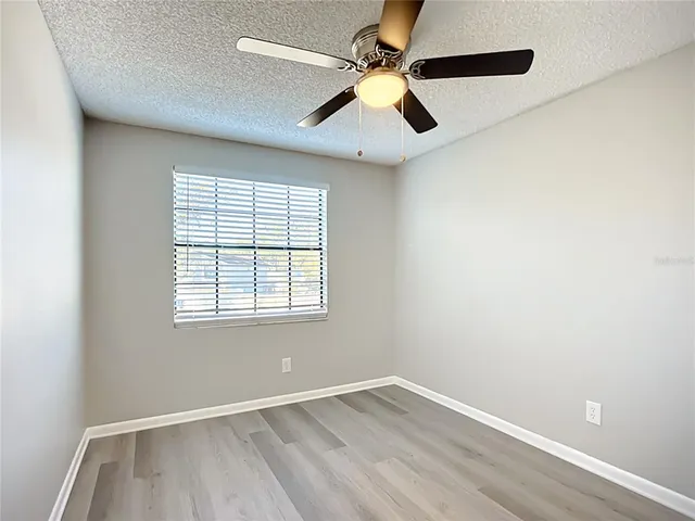 an empty room with wooden floor fan and windows