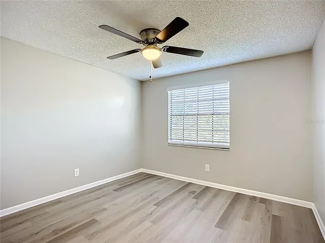 an empty room with wooden floor fan and windows