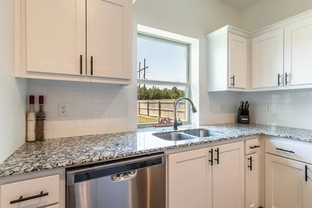 a kitchen with granite countertop a sink stainless steel appliances white cabinets and a window