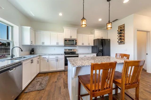 a kitchen with stainless steel appliances granite countertop a kitchen island a stove a refrigerator a sink dishwasher a dining table and chairs with wooden floor