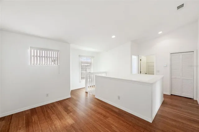 an empty room with a chandelier fan and wooden floor