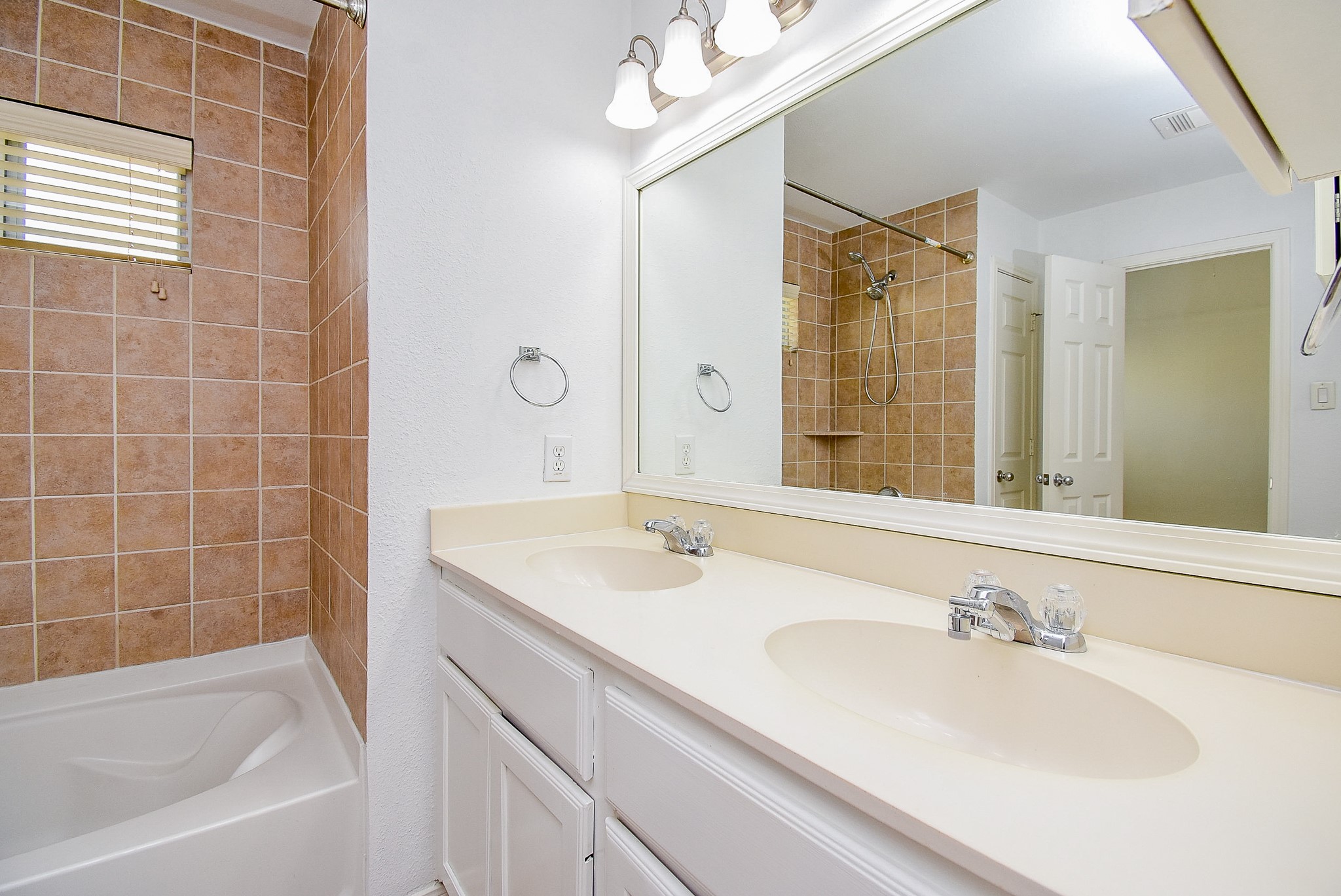 2202 Naomi Street, Unit 3 Houston, TX 77054 - Photo 33 of 42 This bathroom features a dual-sink vanity with a large mirror, warm-toned tile shower and tub, and bright overhead lighting, offering a clean and functional space.