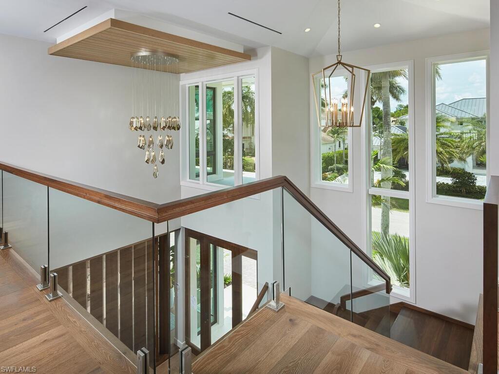 575 17th Avenue South Naples, FL 34102 - Photo 21 of 43 Stairway featuring a healthy amount of sunlight, hardwood / wood-style floors, and an inviting chandelier