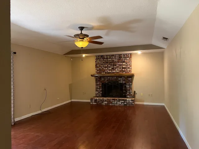 a view of an empty room with wooden floor a fireplace and a window