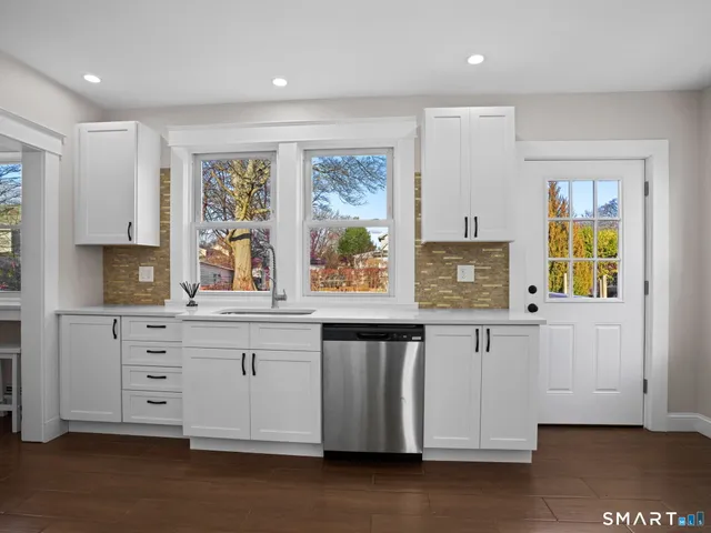 a large white kitchen with granite countertop a stove a sink a window and a dining table