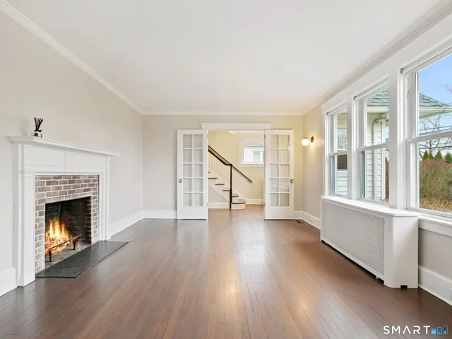a view of an empty room with wooden floor fireplace and a window