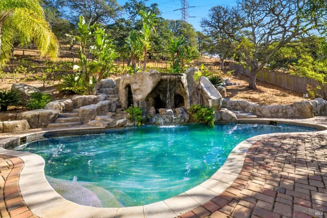 a large white house with a large pool and lawn chairs under an umbrella