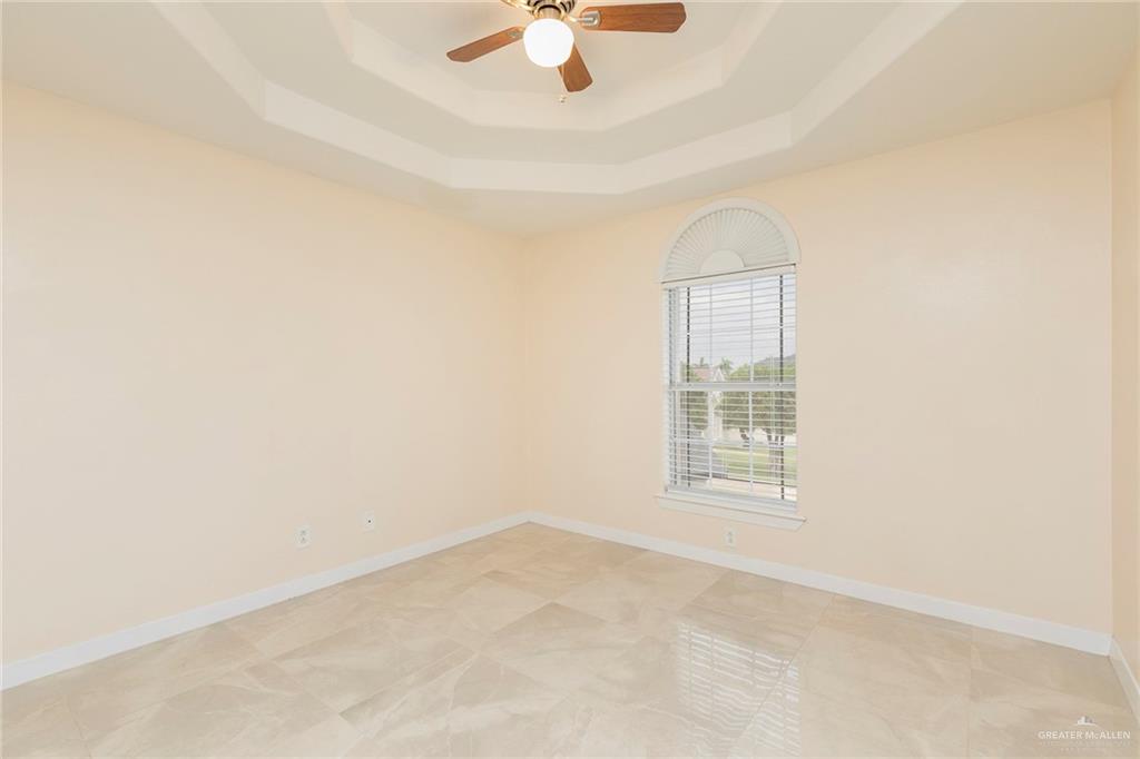 2001 Quail Lane Mission, TX 78572 - Photo 19 of 28 Recessed tray ceiling with a ceiling fan, arched window with horizontal blinds, neutral wall tones, and large format tile flooring