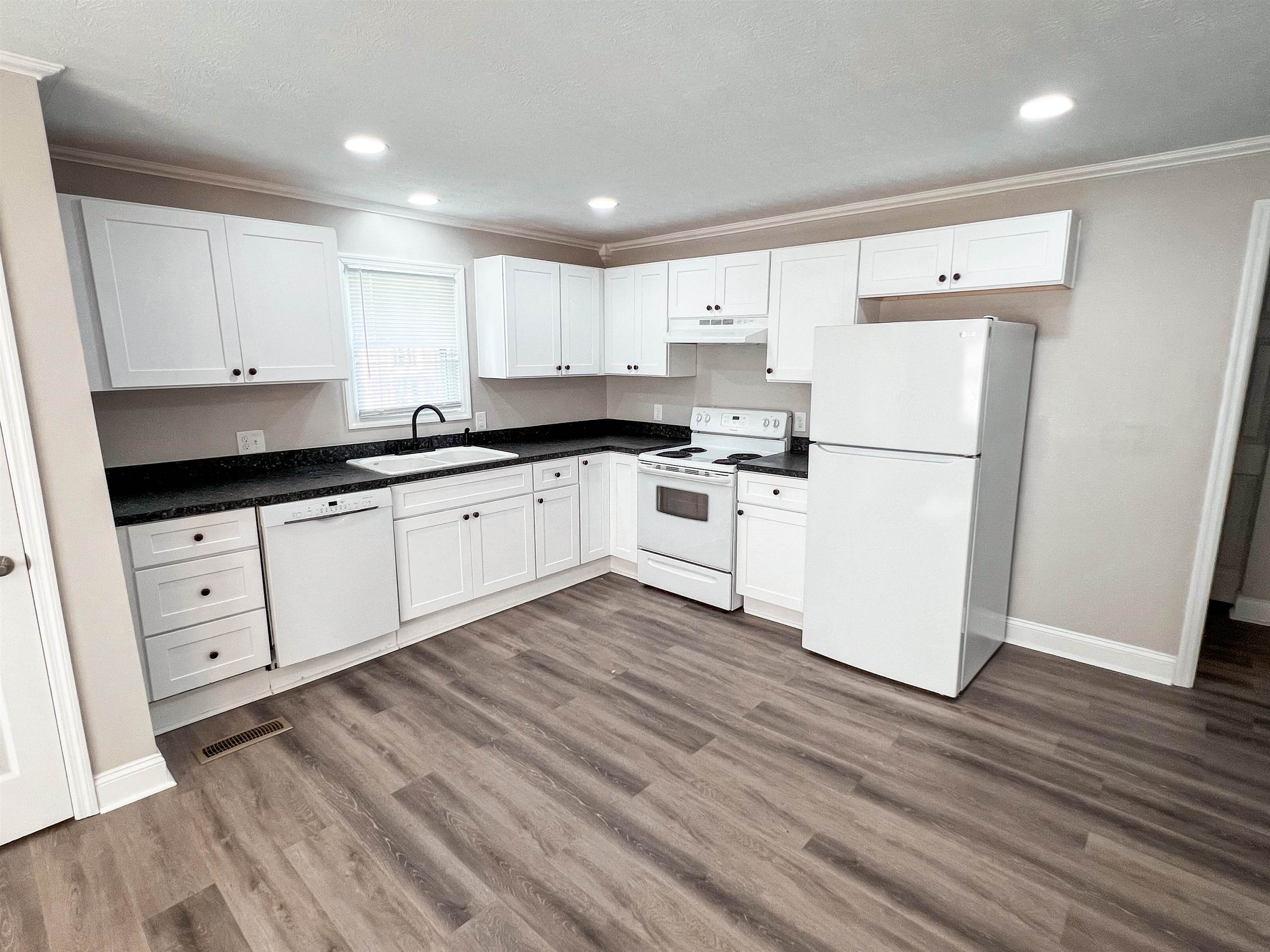 202 Morris Street Waynesboro, TN 38485 - Photo 18 of 36 Kitchen featuring white appliances, crown molding, wood finished floors, dark countertops, and white cabinetry