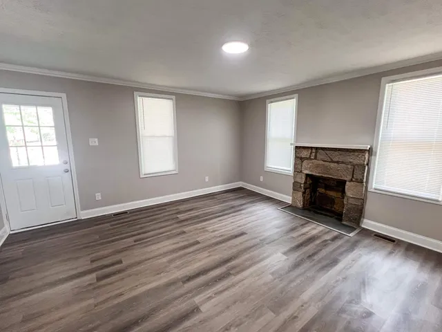 an empty room with wooden floor fireplace and windows