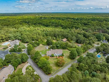 an aerial view of a residential houses with outdoor space and trees all around