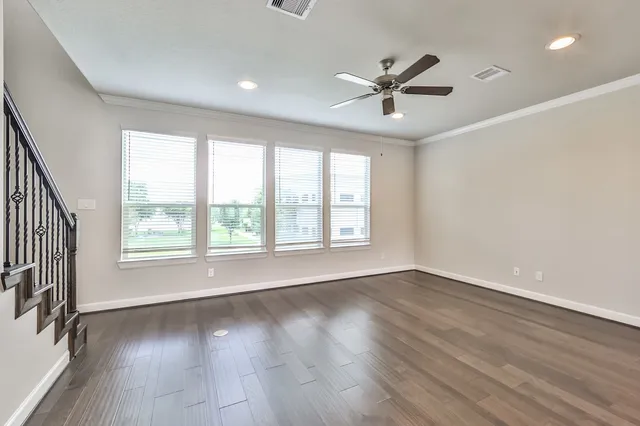 an empty room with wooden floor fan and windows