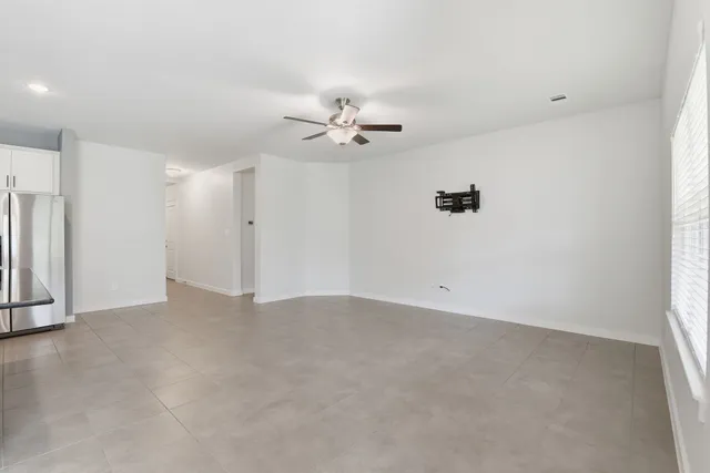 an empty room with chandelier fan and windows