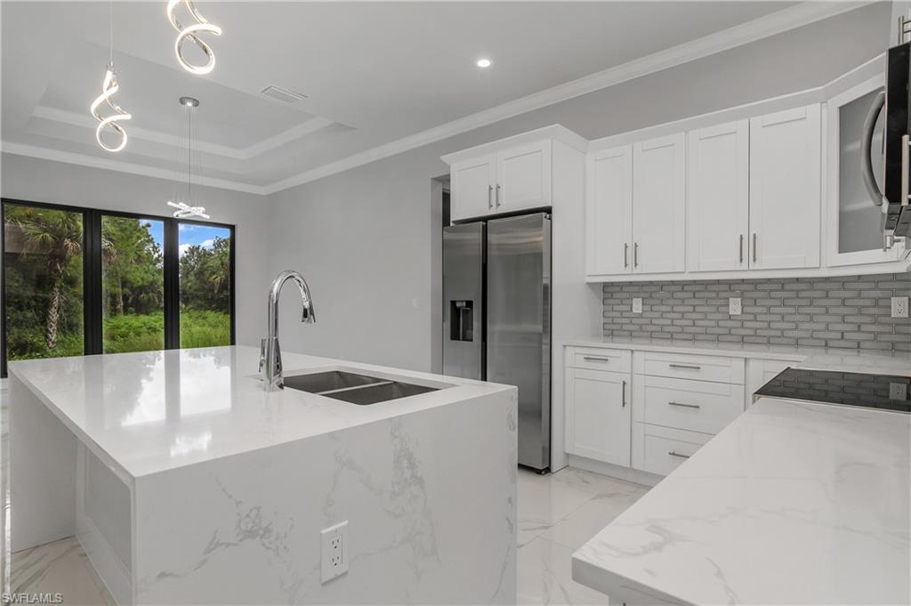 791 14th Street Northeast Naples, FL 34120 - Photo 11 of 46 Kitchen with light stone countertops, decorative light fixtures, stainless steel appliances, crown molding, and an island with sink