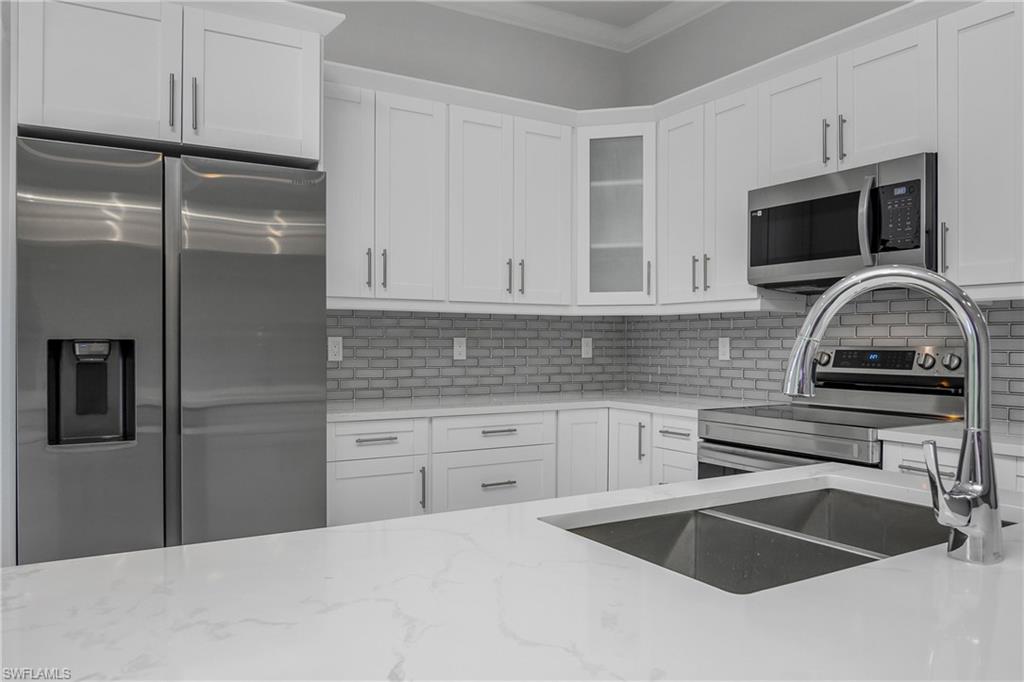 791 14th Street Northeast Naples, FL 34120 - Photo 12 of 46 Kitchen featuring stainless steel appliances, white cabinets, light stone counters, glass fronted cabinets, and decorative backsplash