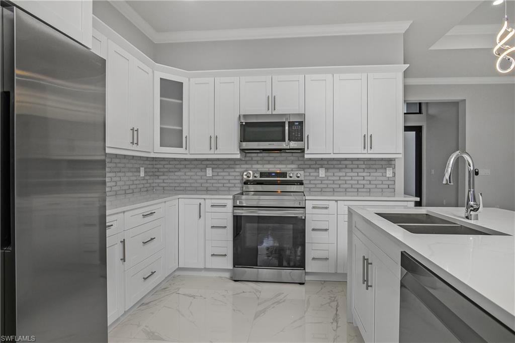 791 14th Street Northeast Naples, FL 34120 - Photo 13 of 46 Kitchen featuring stainless steel appliances, ornamental molding, light stone countertops, and white cabinets