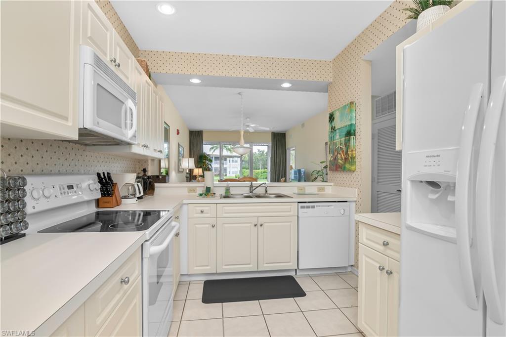 791 14th Street Northeast Naples, FL 34120 - Photo 37 of 46 Kitchen with white appliances, wallpapered walls, light countertops, light tile patterned flooring, and white cabinetry