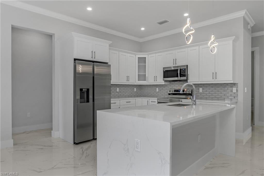 791 14th Street Northeast Naples, FL 34120 - Photo 9 of 46 Kitchen featuring white cabinets, stainless steel appliances, ornamental molding, light stone counters, and hanging light fixtures