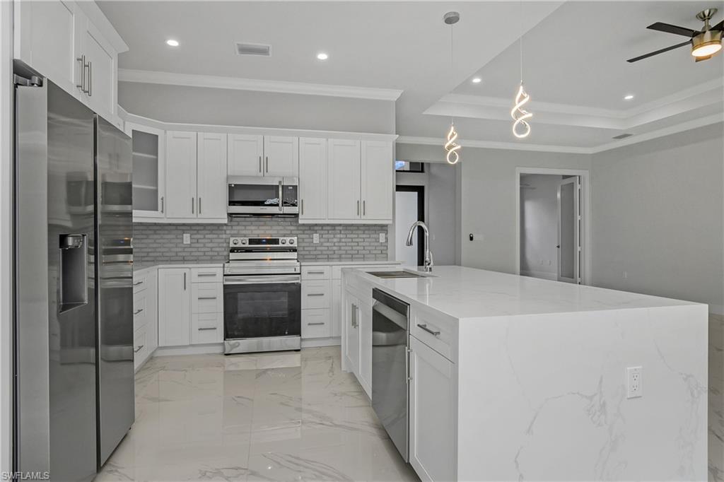 791 14th Street Northeast Naples, FL 34120 - Photo 10 of 46 Kitchen with stainless steel appliances, crown molding, white cabinets, light marble finish floors, and a tray ceiling