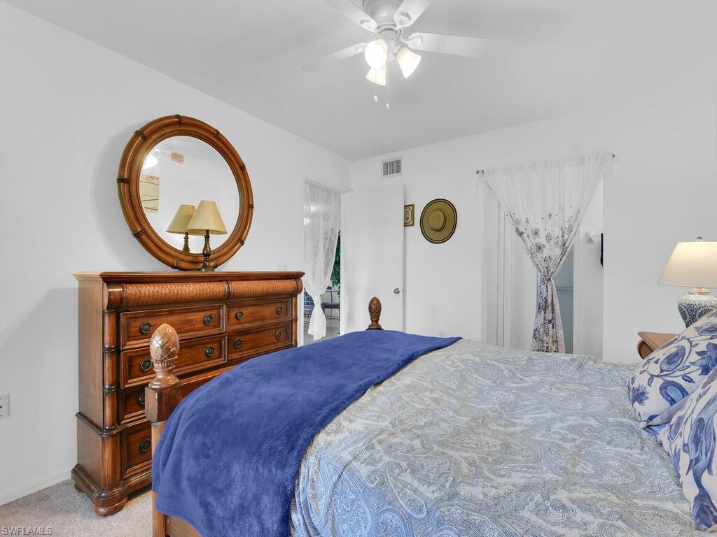 1208 Commonwealth Circle, Unit J102 Naples, FL 34116 - Photo 10 of 21 a bedroom with a bed a mirror and a lamp on dresser