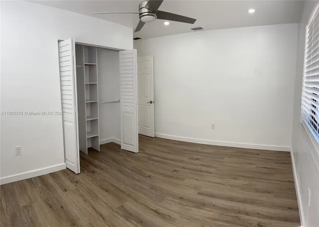 an empty room with wooden floor closet and windows
