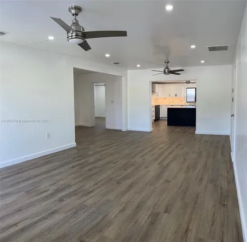 an empty room with wooden floor ceiling fan and kitchen view
