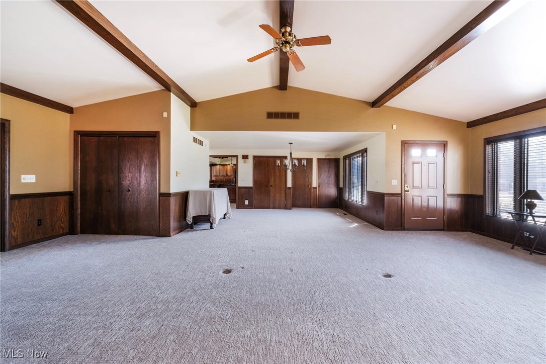 7059 Stewart Sharon Road Hubbard, OH 44425 - Photo 10 of 49 Unfurnished living room with visible vents, vaulted ceiling with beams, carpet floors, wainscoting, and ceiling fan with notable chandelier