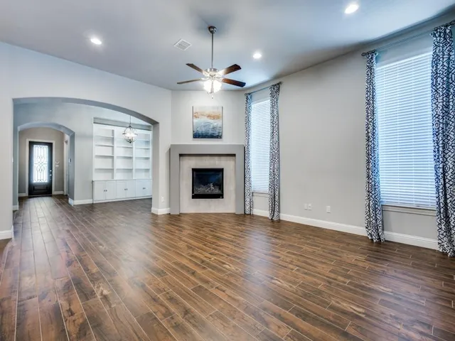 an empty room with wooden floor a ceiling fan and kitchen view