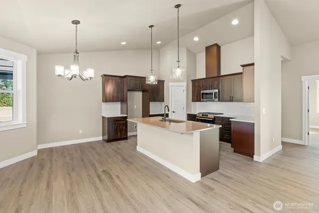 a large kitchen with stainless steel appliances granite countertop a stove a sink dishwasher a refrigerator and a wooden floor