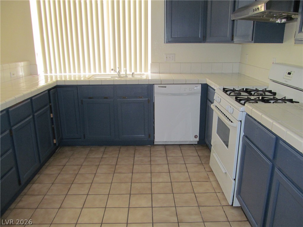 8701 Crescent Ridge Lane Las Vegas, NV 89134 - Photo 8 of 28 A functional kitchen with blue cabinetry and white tile countertops.