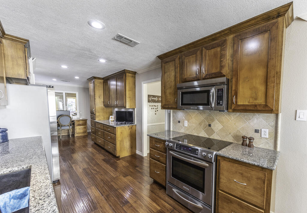 3620 93rd Street Lubbock, TX 79423 - Photo 12 of 33 a kitchen with stainless steel appliances granite countertop a stove top oven a sink dishwasher a refrigerator and cabinets with wooden floor