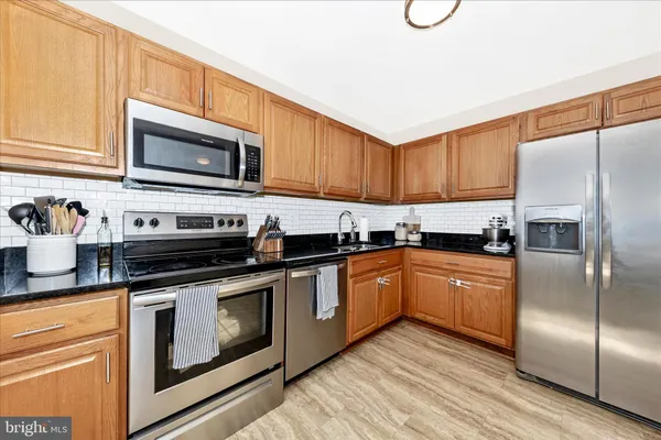 a kitchen with stainless steel appliances granite countertop a refrigerator a stove a sink and dishwasher with wooden floor