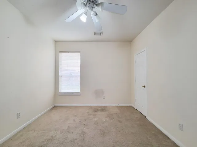 an empty room with a chandelier fan and windows