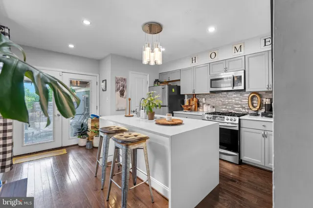 a kitchen with kitchen island granite countertop a stove a sink a refrigerator and white cabinets with wooden floor