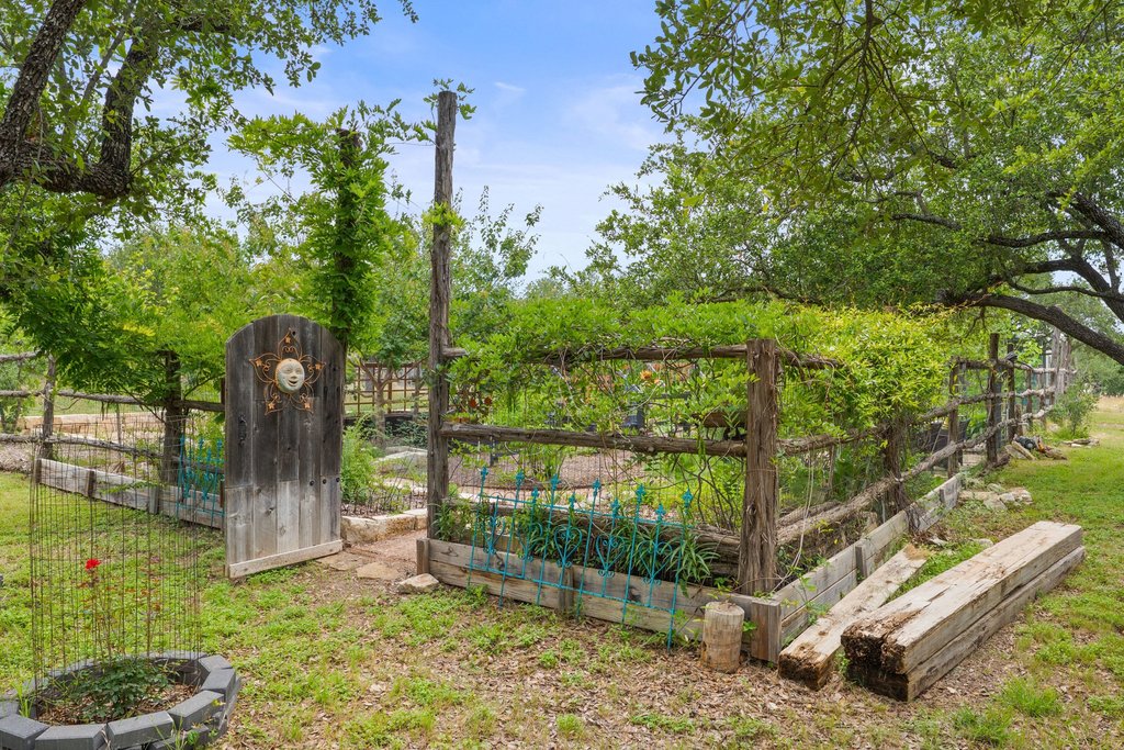 290 Sunset Ridge Dripping Springs, TX 78620 - Photo 6 of 37 A charming wooden gate and fence lead into a verdant garden space, enclosed by flourishing trees and natural greenery.