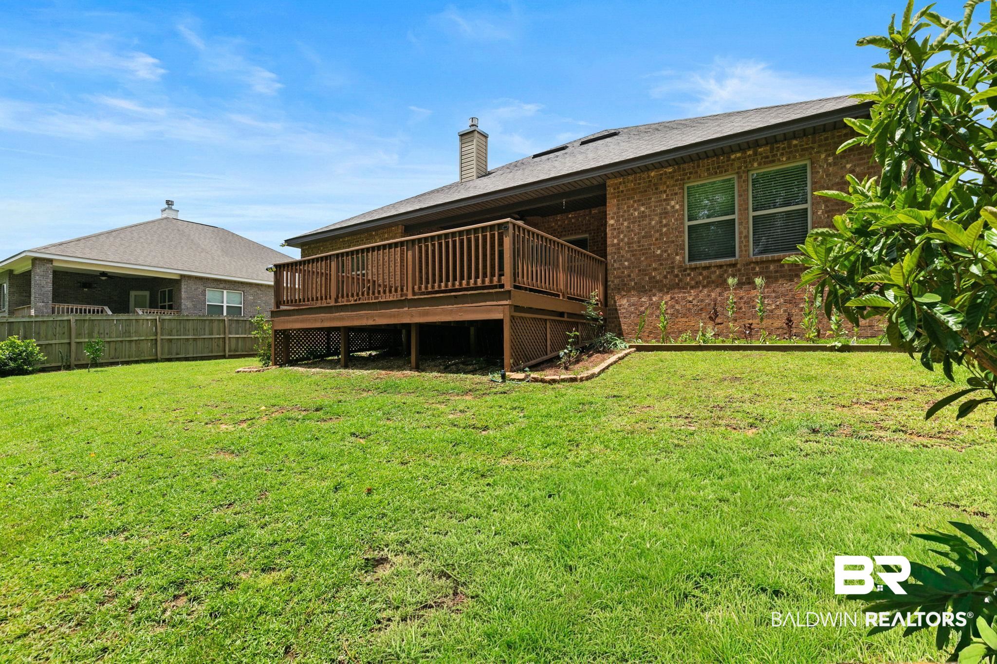 31350 Hoot Owl Road Daphne, AL 36527 - Photo 91 of 94 Spacious green lawn featuring a raised wooden deck with lattice skirting, brick exterior, and a privacy fence