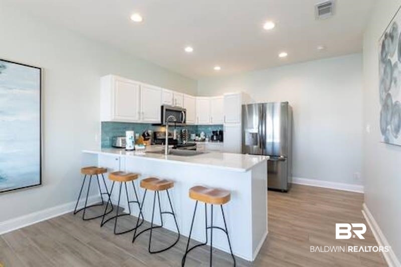 1492 Shell Lane Gulf Shores, AL 36542 - Photo 5 of 20 Kitchen with appliances with stainless steel finishes, a peninsula, a breakfast bar, decorative backsplash, and light wood finished floors