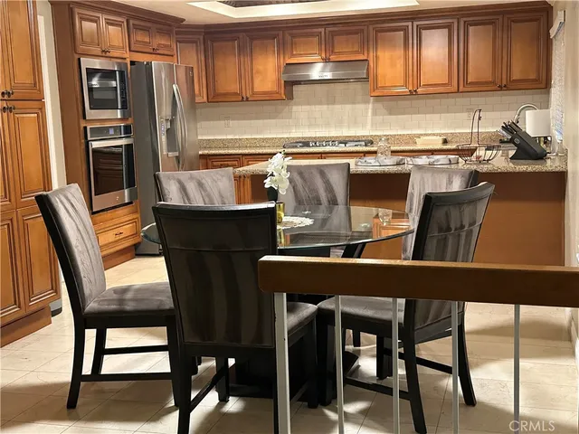 a kitchen with stainless steel appliances granite countertop a dining table chairs refrigerator and sink